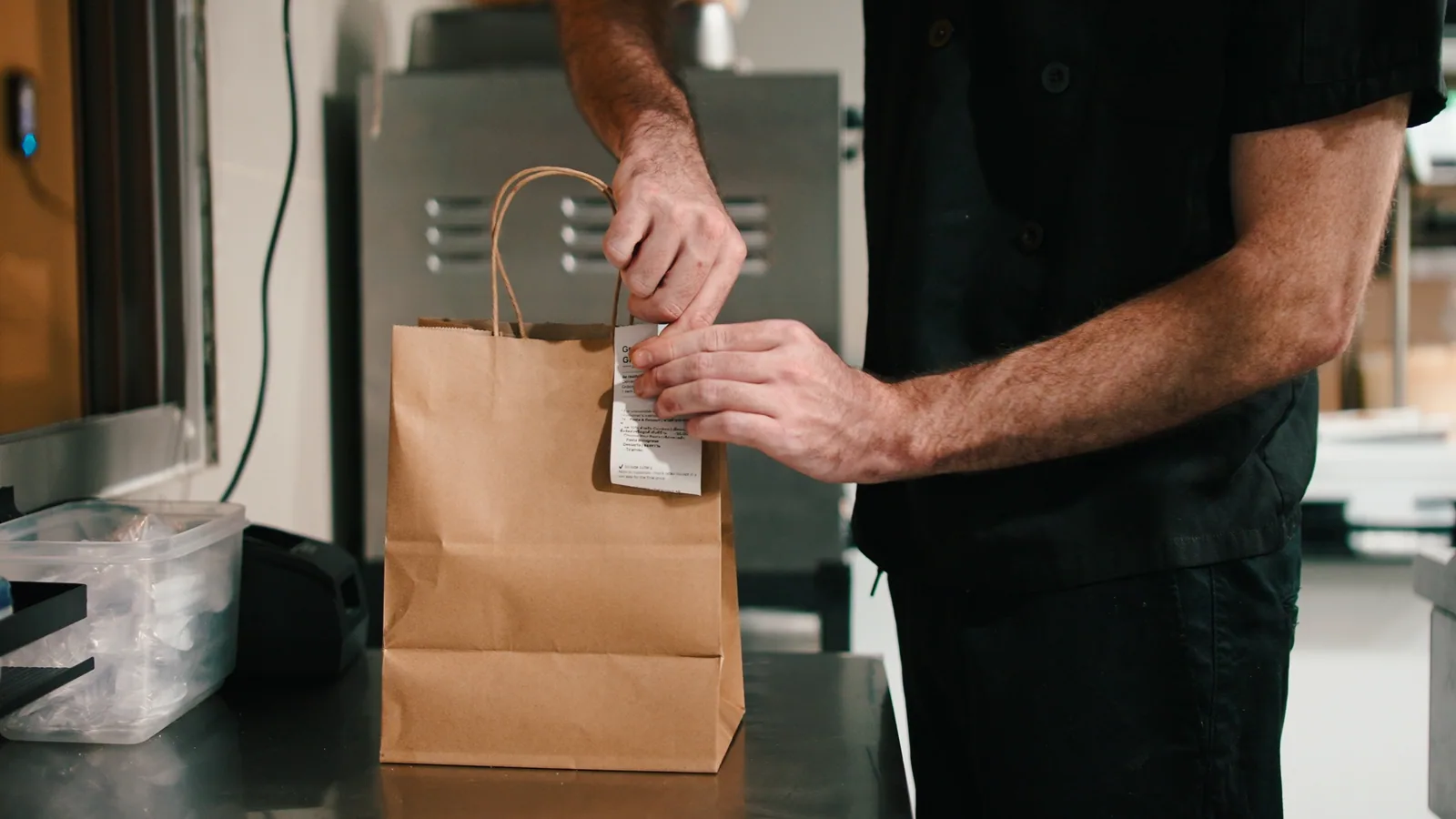 A restaurant team member sealing a prepared delivery order in the kitchen